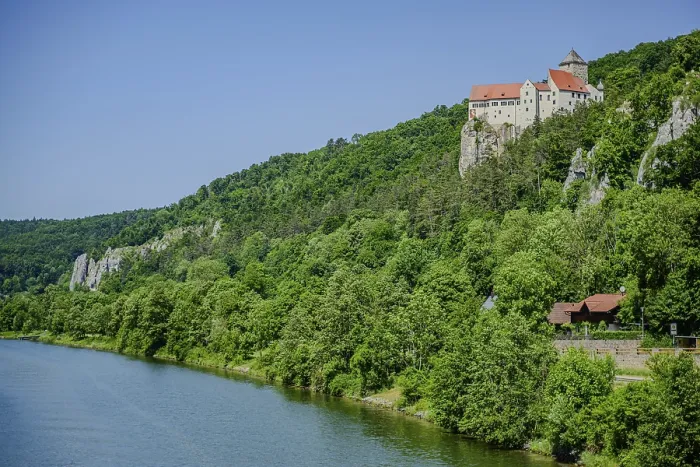 Framed Print : A castle towers over a river in the midst of a green forest and rocks