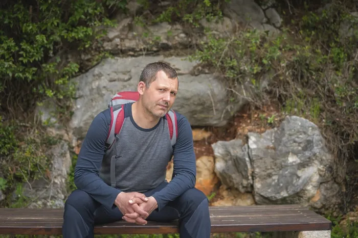 Framed Print : Caucasian male with a backpack pausing to rest on a bench while walking on a path in a forest on a coastal trail