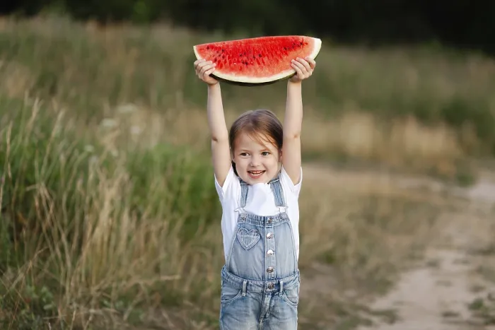 Framed Print : A cheerful child holds a slice of watermelon above their head