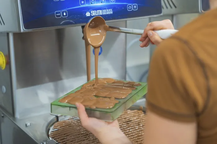Framed Print : Chocolate is filled into flat molds by a person from a device Framed Print : Chocolate is filled into flat molds by a person from a device
