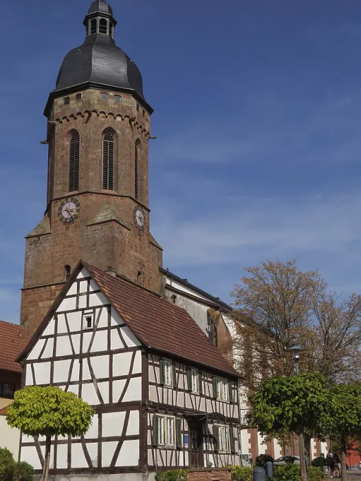 Framed Print : A church tower towers over a traditional half-timbered house under a bright blue sky