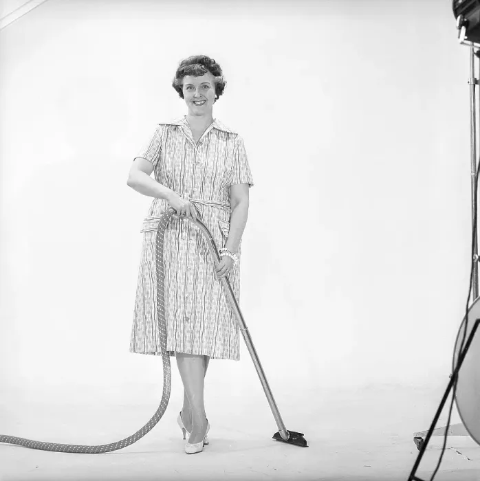 Framed Print : Cleaning day in the 1960s. A woman is standing holding a vacuum cleaner