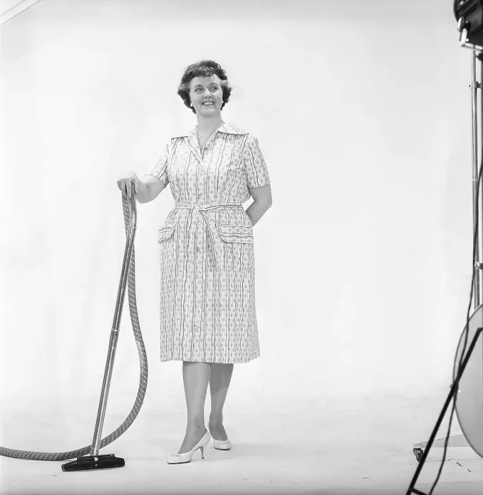 Framed Print : Cleaning day in the 1960s. A woman is standing holding a vacuum cleaner