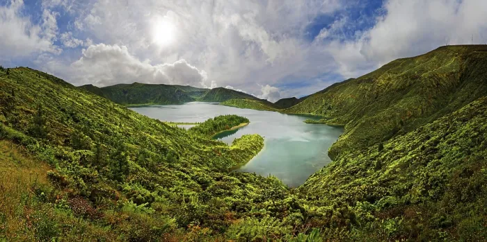 Framed Print : A clear lake surrounded by green hills and mountains under a blue sky with clouds on a sunny day