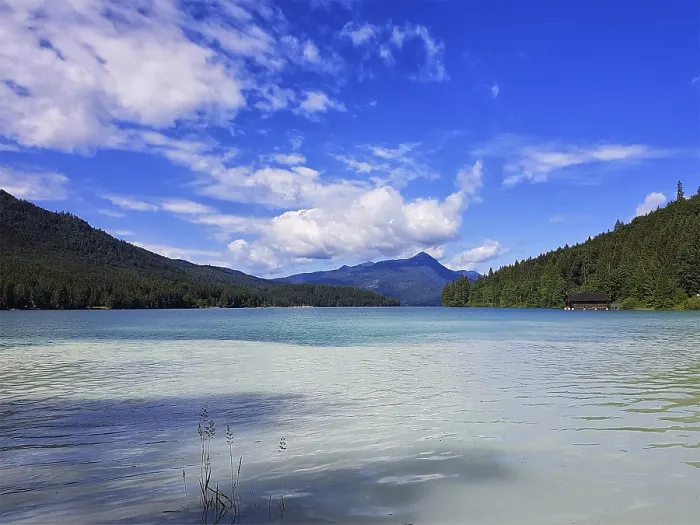 Framed Print : A clear lake with surrounding mountains and wooded slopes under a blue sky with white clouds Framed Print : A clear lake with surrounding mountains and wooded slopes under a blue sky with white clouds