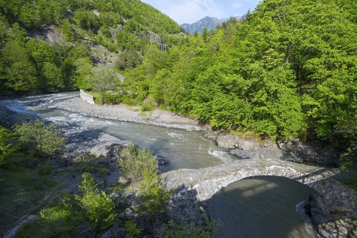 Framed Print : A clear river flows under an old stone bridge through a green