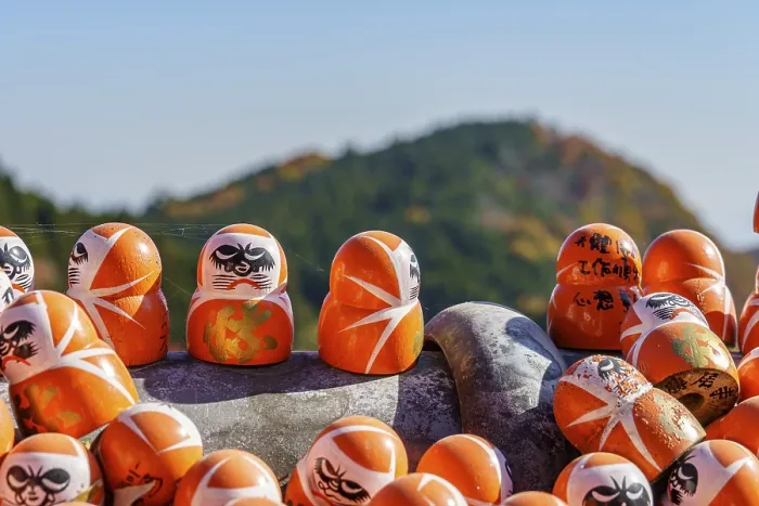 Framed Print : Close-up of Daruma figures with an autumnal mountain in the background and clear sky