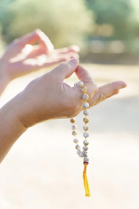 Framed Print : Close-up of a woman's hands holding a sunlit Buddhist mala praying in a field at sunset Close-up of a woman's