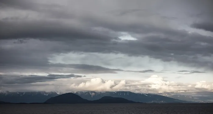 Framed Print : Clouds hover over distant mountains and sea in a moody landscape as seen from a passenger ferry Framed Print : Clouds hover over distant mountains and sea in a moody landscape as seen from a passenger ferry