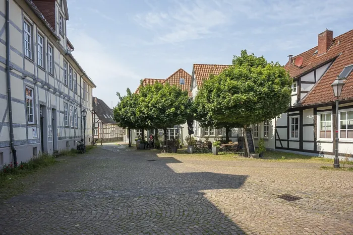 Framed Print : Cobbled courtyard with traditional half-timbered houses and trees on a sunny day