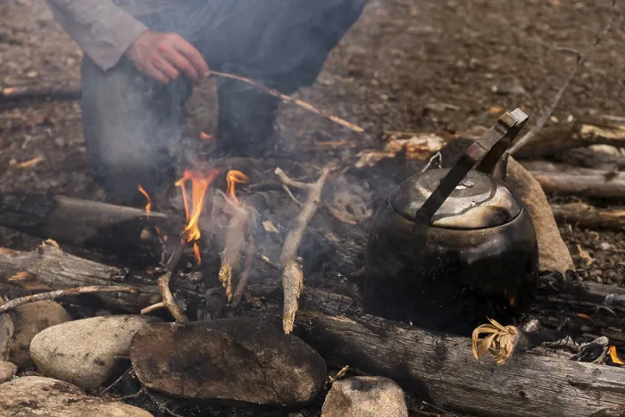 Framed Print : Coffee kettle on the campfire, behind it the legs of a person kneeling at the campfire Framed Print : Coffee kettle on the campfire, behind it the legs of a person kneeling at the campfire