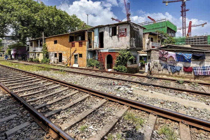 Framed Print : Construction cranes rise behind brightly painted houses along the train tracks under a blue sky