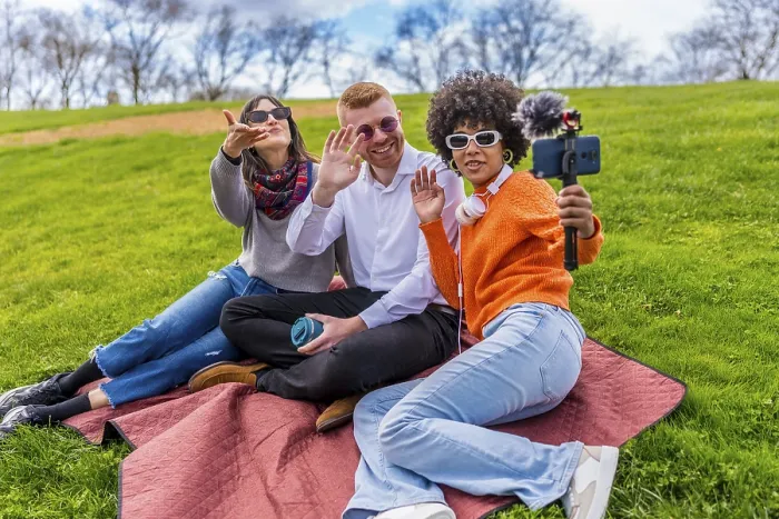 Framed Print : Three content creators waving and filming video with smartphone and external microphone in a park