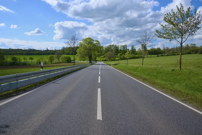 Framed Print : Country road through green fields and trees under a slightly cloudy sky