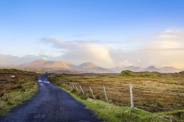 Framed Print : Empty country road between meadows leading to mountains in far distance