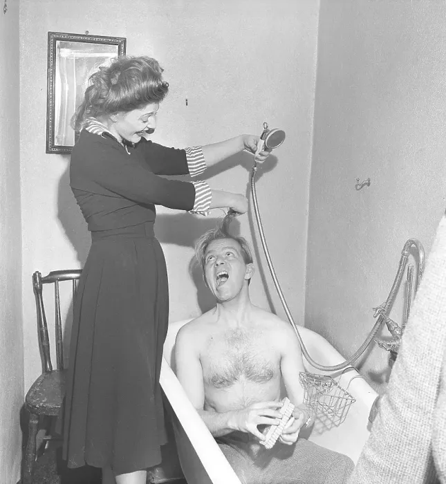 Framed Print : Couple in the bathroom in the 1940s. A man sits in a bathtub with only his pants on. A young woman laughs and playfully holds his hair and the shower head to pretend to shower him. Sweden 1949. Kristoffersson ref AT43-4