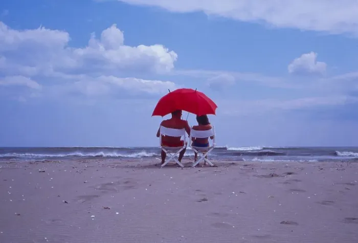 Framed Print : Couple on the beach, seated under red sunshade
