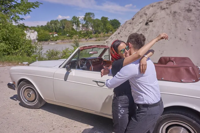 Framed Print : A couple embracing joyfully by a white convertible car on a sunny day next to building site of work