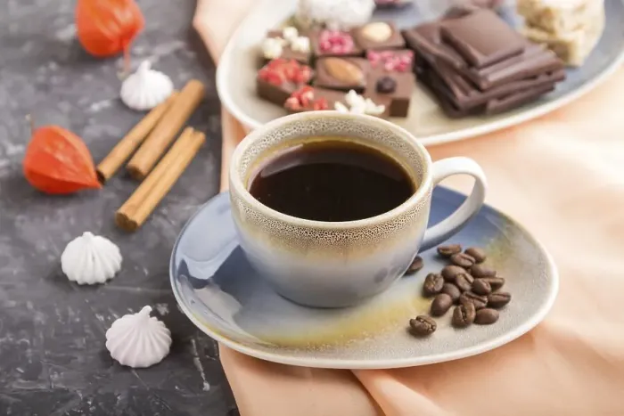 Framed Print : A cup of coffee with chocolate and coconut candies on a black concrete background and orange textile