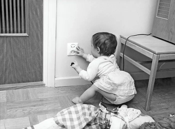 Framed Print : Dangerous in the 1960s. A child is sitting on the floor and is curious about the electrical outlet in the wall. She holds a plug in one hand and fingers the outlet with the other Framed Print : Dangerous in the 1960s. A child is sitting on the floor and is curious about the electrical outlet in the wall. She holds a plug in one hand and fingers the outlet with the other