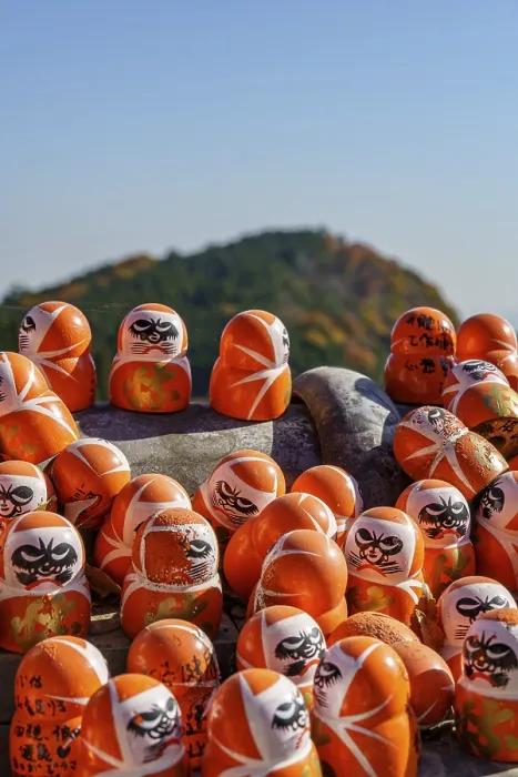 Framed Print : Several Daruma figures in front of an autumnal mountain and a blue sky Framed Print : Several Daruma figures in front of an autumnal mountain and a blue sky
