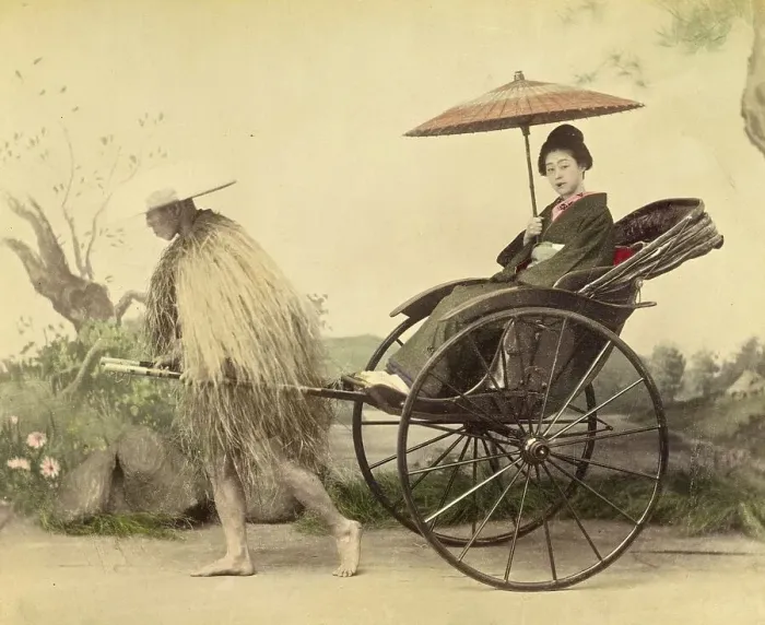 Framed Print : A distinguished woman with a parasol being pulled in a jinrikisha by a man wearing a straw mackintosh