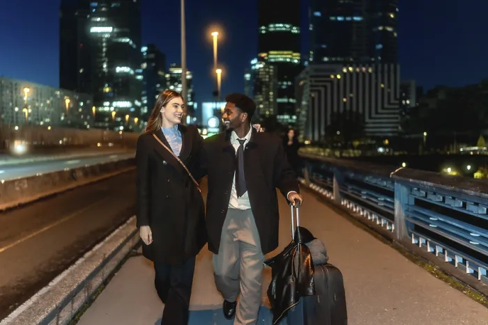 Framed Print : Diverse couple walking together holding hands and pulling a suitcase in a modern urban city district at night Framed Print : Diverse couple walking together holding hands and pulling a suitcase in a modern urban city district at night