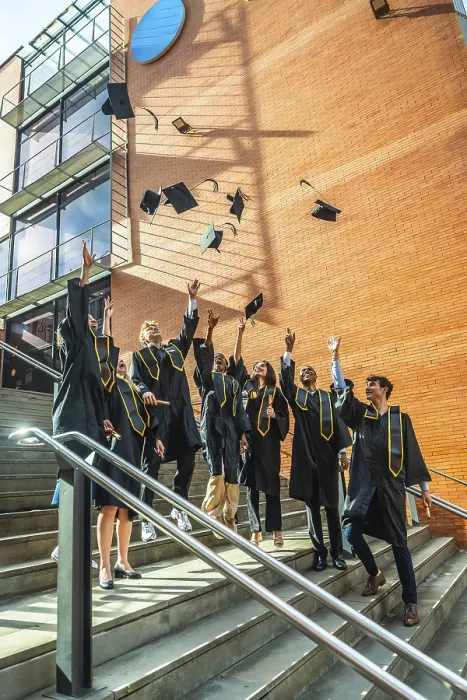 Framed Print : Diverse group of young adult university graduates celebrating a successful academic achievement by tossing their Framed Print : Diverse group of young adult university graduates celebrating a successful academic achievement by tossing their