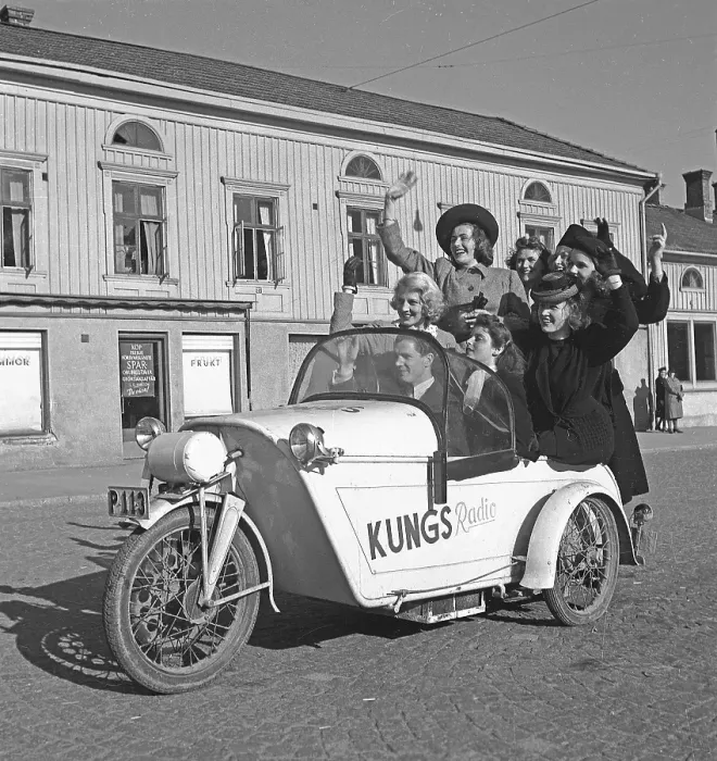 Framed Print : Driving in the 1940s. A man drives a three wheeled motorcycle and a group of women have joined the ride