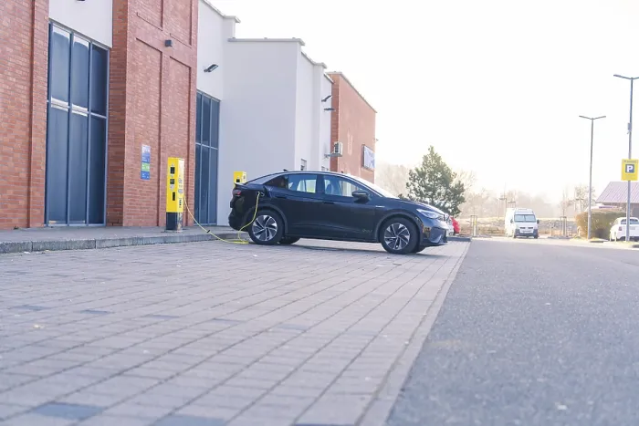 Framed Print : An electric car charging in a car park in front of a modern building in daylight Framed Print : An electric car charging in a car park in front of a modern building in daylight