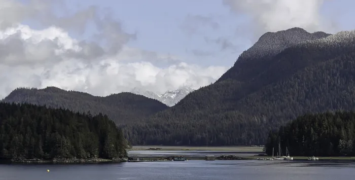 Framed Print : An expansive view of a lake bordered by forests and mountains under a cloudy sky in Tofino