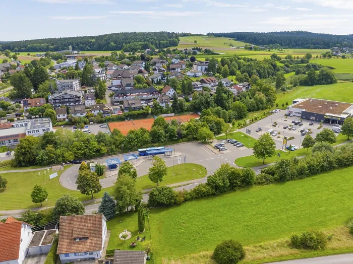 Framed Print : Far-reaching view of a village with green fields and a central car park under a blue sky Framed Print : Far-reaching view of a village with green fields and a central car park under a blue sky