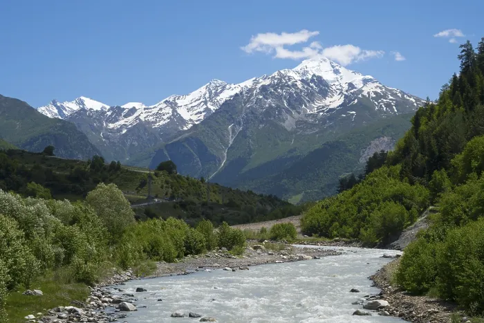 Framed Print : Fast-flowing river in a wooded valley against a backdrop of snow-capped mountains
