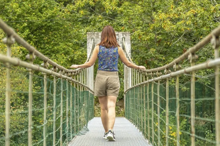 Framed Print : Female tourist enjoying a peaceful walk across a metallic hanging bridge