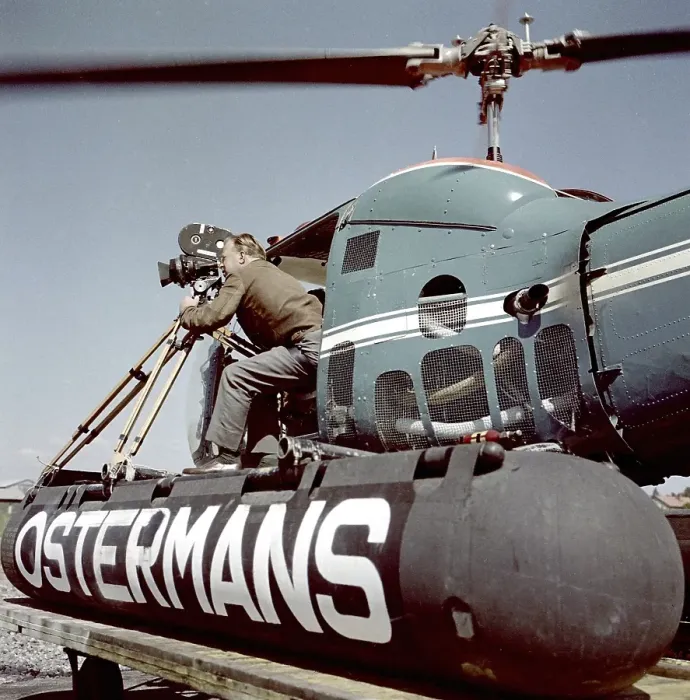 Framed Print : Filming in the 1950s. A cinematographer is standing half way out of a helicopter when filming something. The film camera is mounted on a tripod. Ostermans was a swedish company specialized in helicopter transports