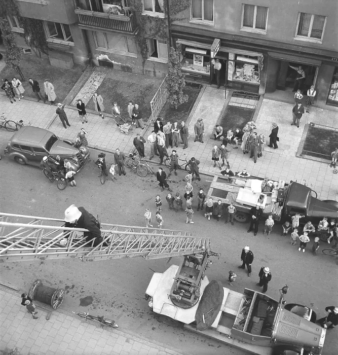 Framed Print : Fireman 1946 A fire engine is standing in the street with the ladder raised towards the house where a fireman can be seen climbing up. People are gathered in the street looking up at the fireman. Kristoffersson 1946 ref U81-3