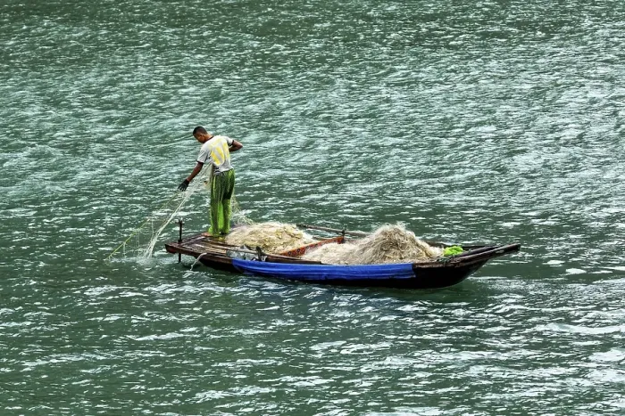 Framed Print : A fisherman pulls a large net from a small boat onto the water