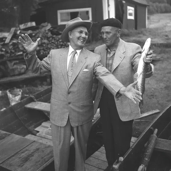 Framed Print : Fishing in the 1950s. A man has caught a fish and shows it up for his friend Framed Print : Fishing in the 1950s. A man has caught a fish and shows it up for his friend