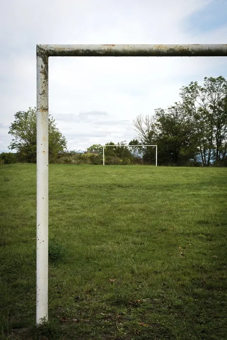 Framed Print : Football goalpost in a grassy field under a cloudy sky near a rural area