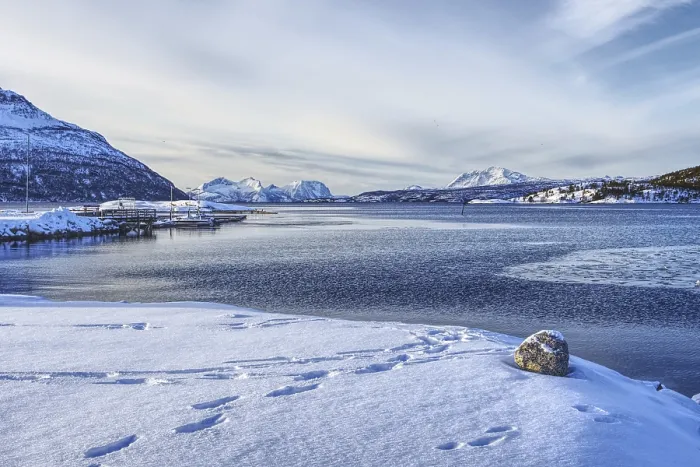 Framed Print : Footprints in the snow on the beach with a view of the sea and mountains under a blue sky