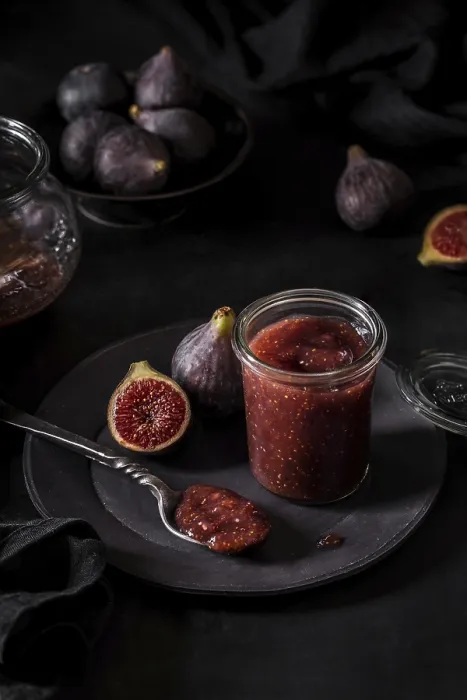 Framed Print : From above fresh fruit jam in small jar and on spoon with full and cut figs on plate at black kitchen table