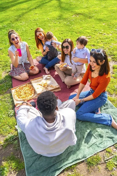 Framed Print : Friends and their babies are sharing pizza and drinks during a cheerful picnic in a park