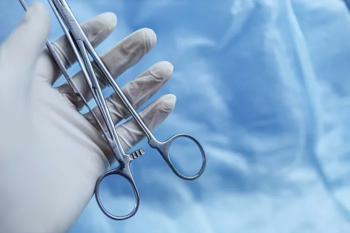 Framed Print : A gloved hand holding surgical tools against a soft blue background Framed Print : A gloved hand holding surgical tools against a soft blue background