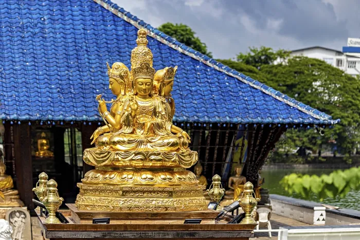 Framed Print : Golden Buddhist statue in front of a blue roof with cloudy sky