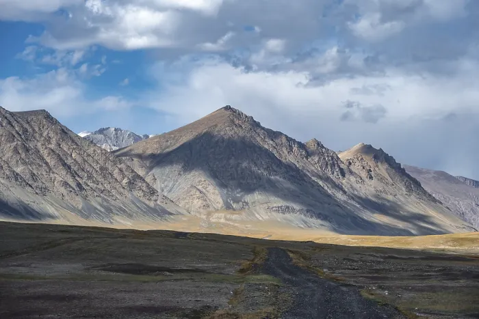 Framed Print : Gravel track on plateau, dramatic high mountains