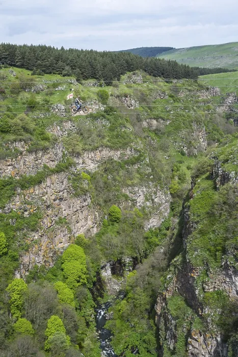 Framed Print : A green gorge with rocks and trees crossed by a small river under a cloudy sky