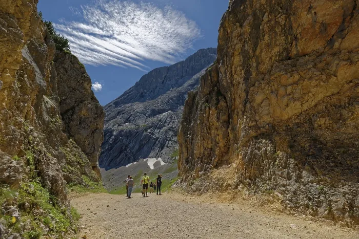 Framed Print : A group of hikers on a mountain path surrounded by imposing rocks under a blue sky with foehn clouds