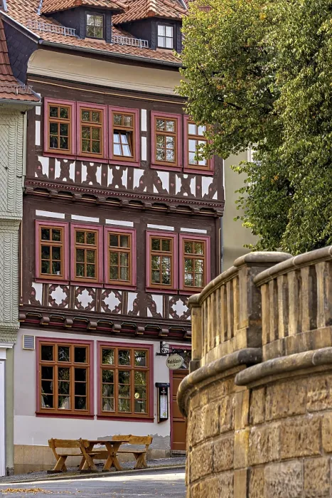 Framed Print : A half-timbered house with red window frames next to a stone wall in a historic town