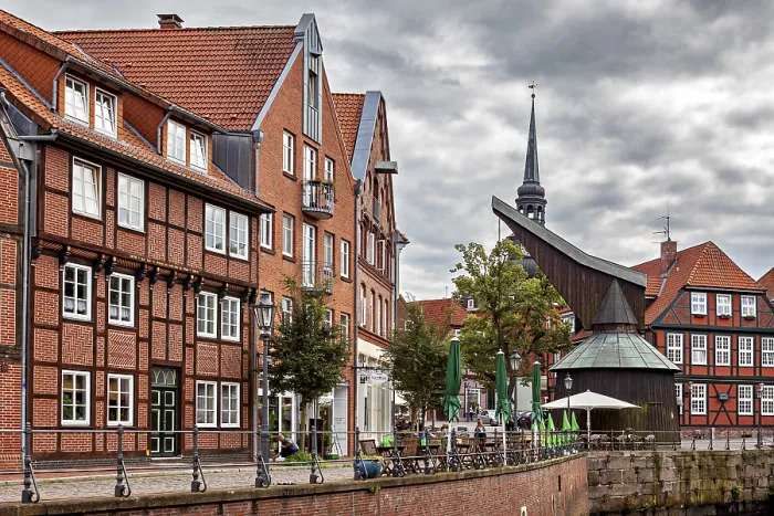 Framed Print : Half-timbered houses and a decorated tower on a riverbank with terraces and cloudy sky Framed Print : Half-timbered houses and a decorated tower on a riverbank with terraces and cloudy sky