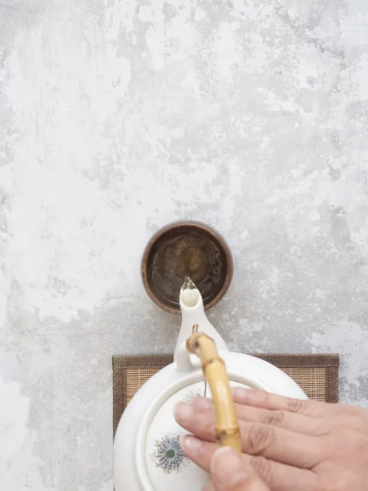 Framed Print : Hand gracefully pours tea from a white ceramic teapot with bamboo handle into a small brown bowl on a textured gray Framed Print : Hand gracefully pours tea from a white ceramic teapot with bamboo handle into a small brown bowl on a textured gray